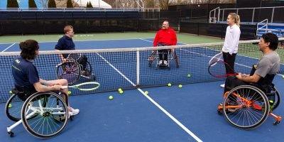 Four wheelchair players and a coach at the net during a clinic