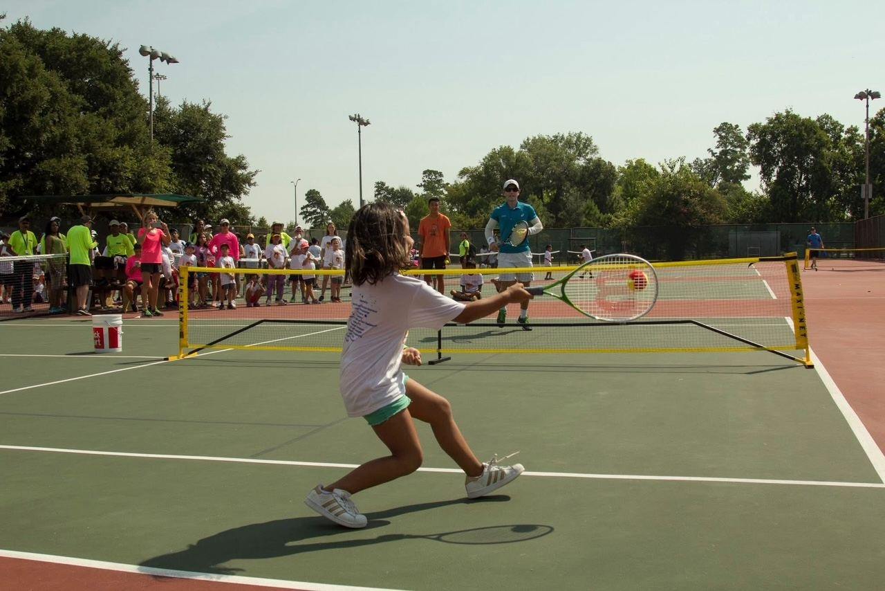 A girl hitting a forehand over a short-court net while other children watch
